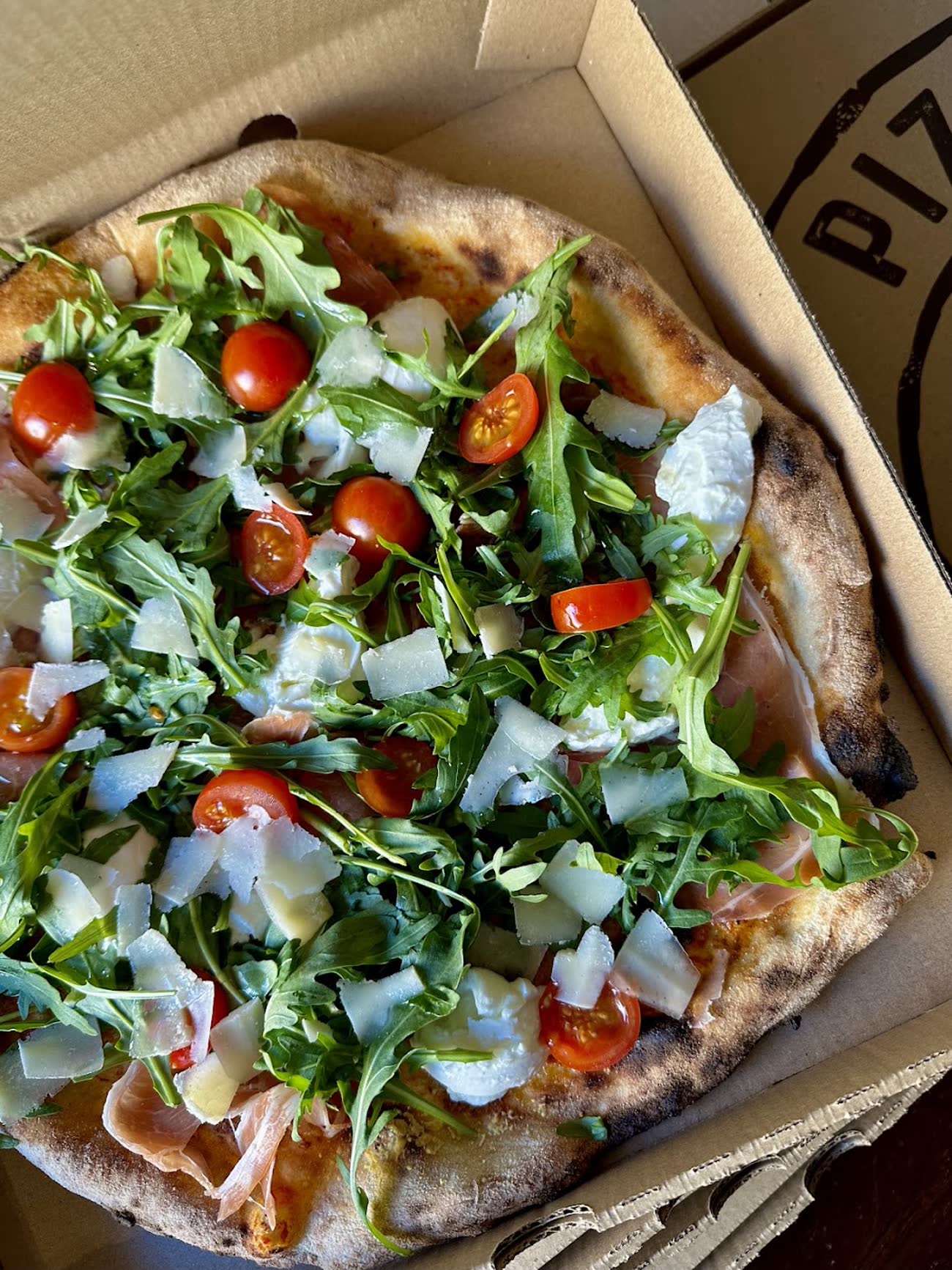 Pizza con rúcula, tomate cherry, mozzarella de búfala y jamón serrano recién salida del horno